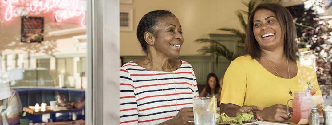 Ratgeber Makula: Zwei Frauen im Café unterhalten sich Zwei Frauen in einem Café unterhalten sich. Beide lachen.