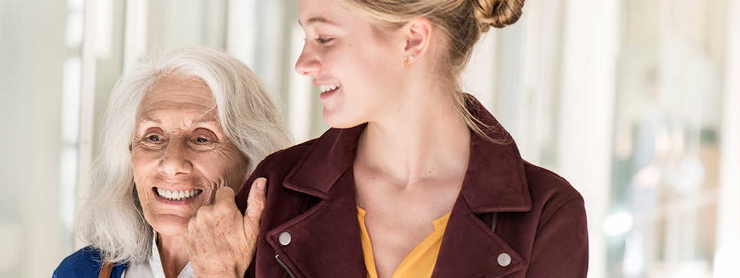 Eine ältere Dame hält sich an ihrer Enkelin fest. Beide lachen.