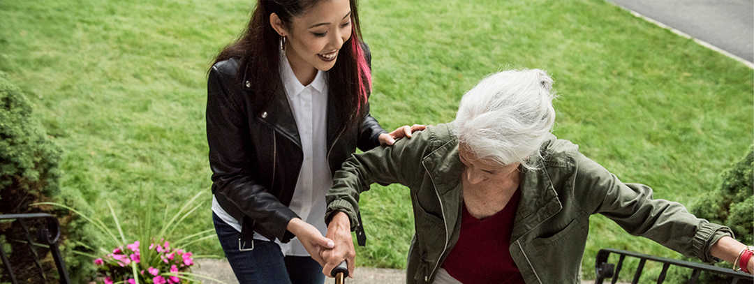 Eine junge Frau hilft einer älteren beim Treppensteigen an einem Hauseingang