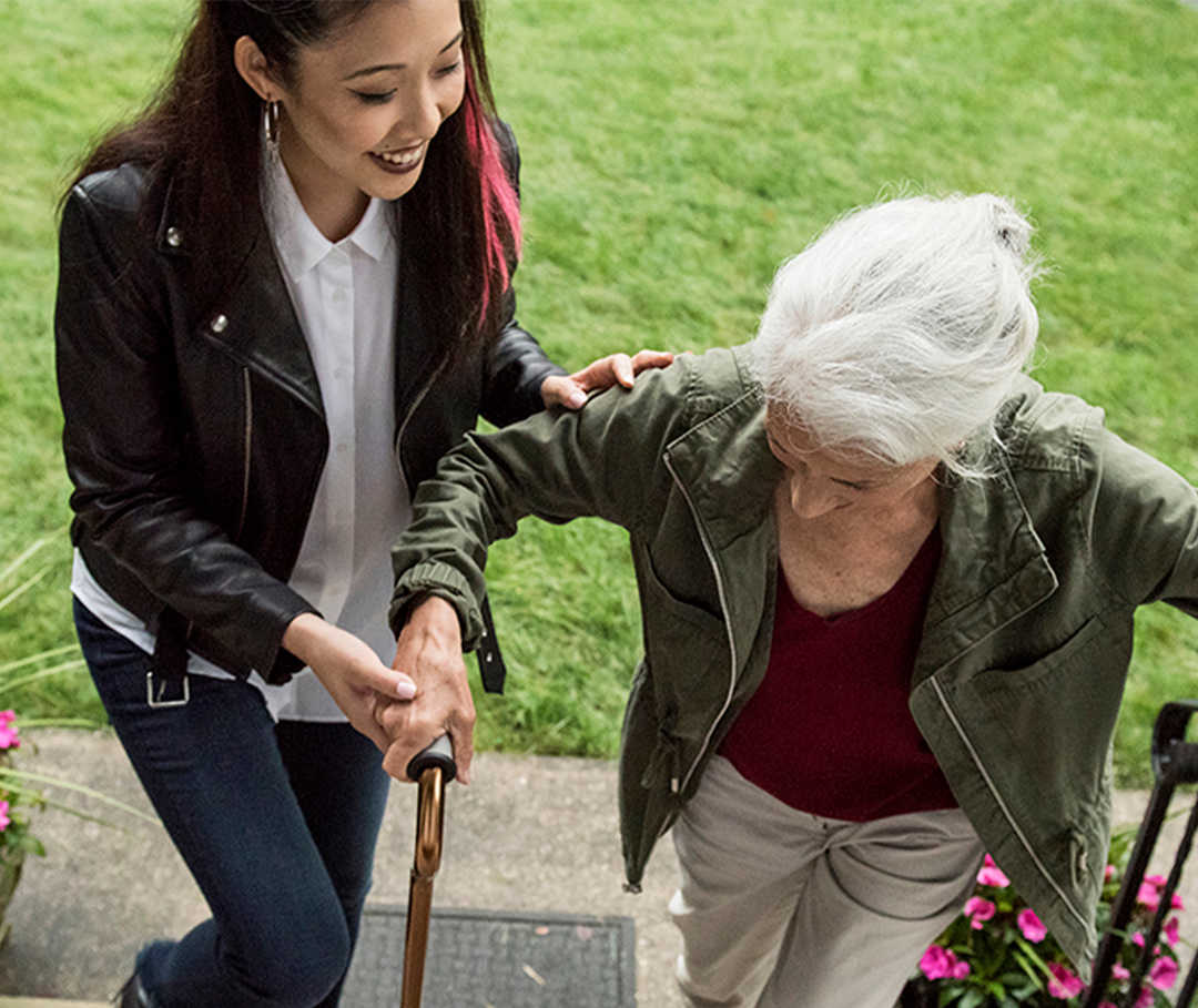 Eine junge Frau hilft einer älteren beim Treppensteigen an einem Hauseingang
