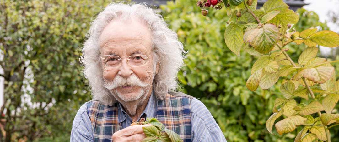 Jean Pütz steht in seinem Garten und blickt lächelnd in die Kamera.