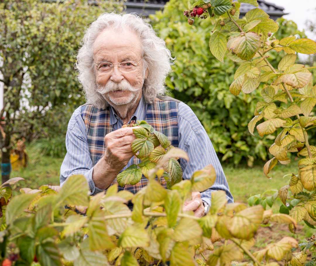 Jean Pütz steht in seinem Garten und blickt lächelnd in die Kamera.
