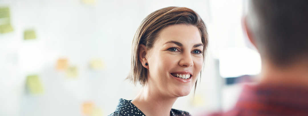 Eine Frau vor einer weißen Tafel bespricht etwas mit einem Kollegen.